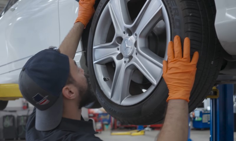 Mechanic in a cap inspects a car tire, wearing orange gloves, in an auto workshop