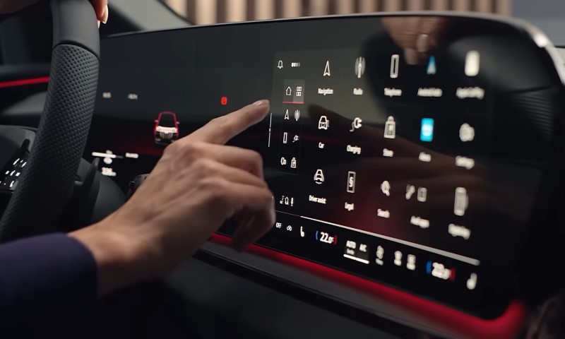 A hand interacts with a car's sleek modern touchscreen dashboard displaying navigation and various control icons