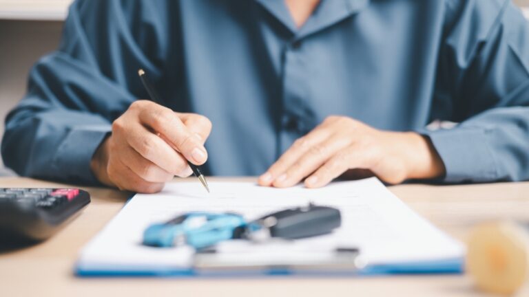 Person signing vehicle registration paperwork with car keys and calculator on the desk