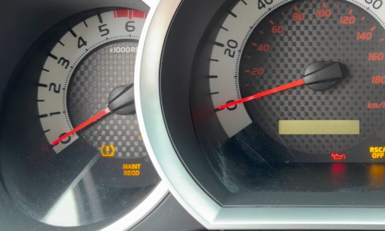 Close-up of a car dashboard showing a tachometer and speedometer with warning lights on. The "Maintenance Required" and oil warning lights are illuminated