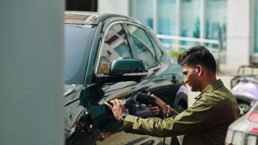 Man charging a black electric car in a parking area near an office building