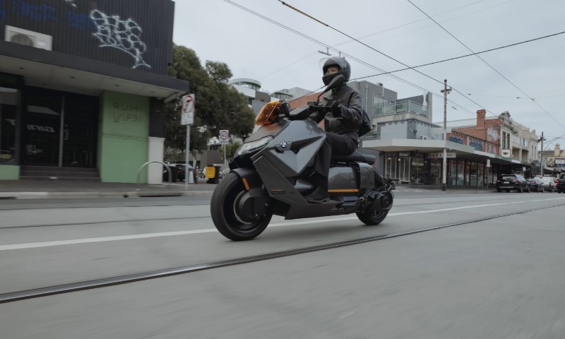 A person rides a sleek, futuristic gray scooter on an urban street
