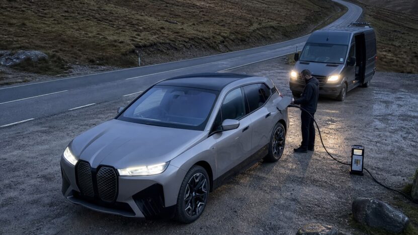 Electric SUV at a roadside pull-off connected to a portable charger from an unmarked assistance van