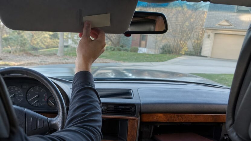 Driver tucks an unmarked assistance card into the visor of an older sedan in a driveway